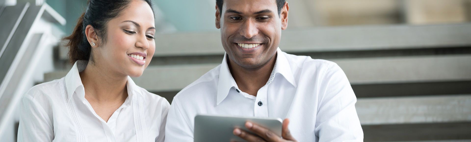 Two colleagues smiling while reviewing content on a tablet together.