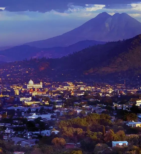 San Salvador cityscape at dusk with a prominent mountain in the background.