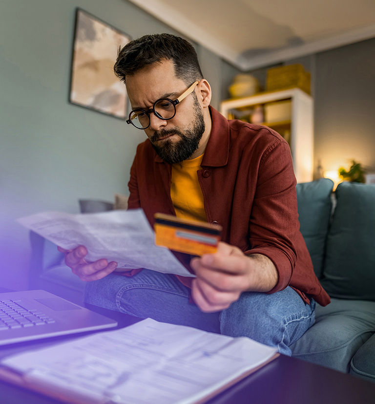 Man reviewing a bill while holding a credit card at home.